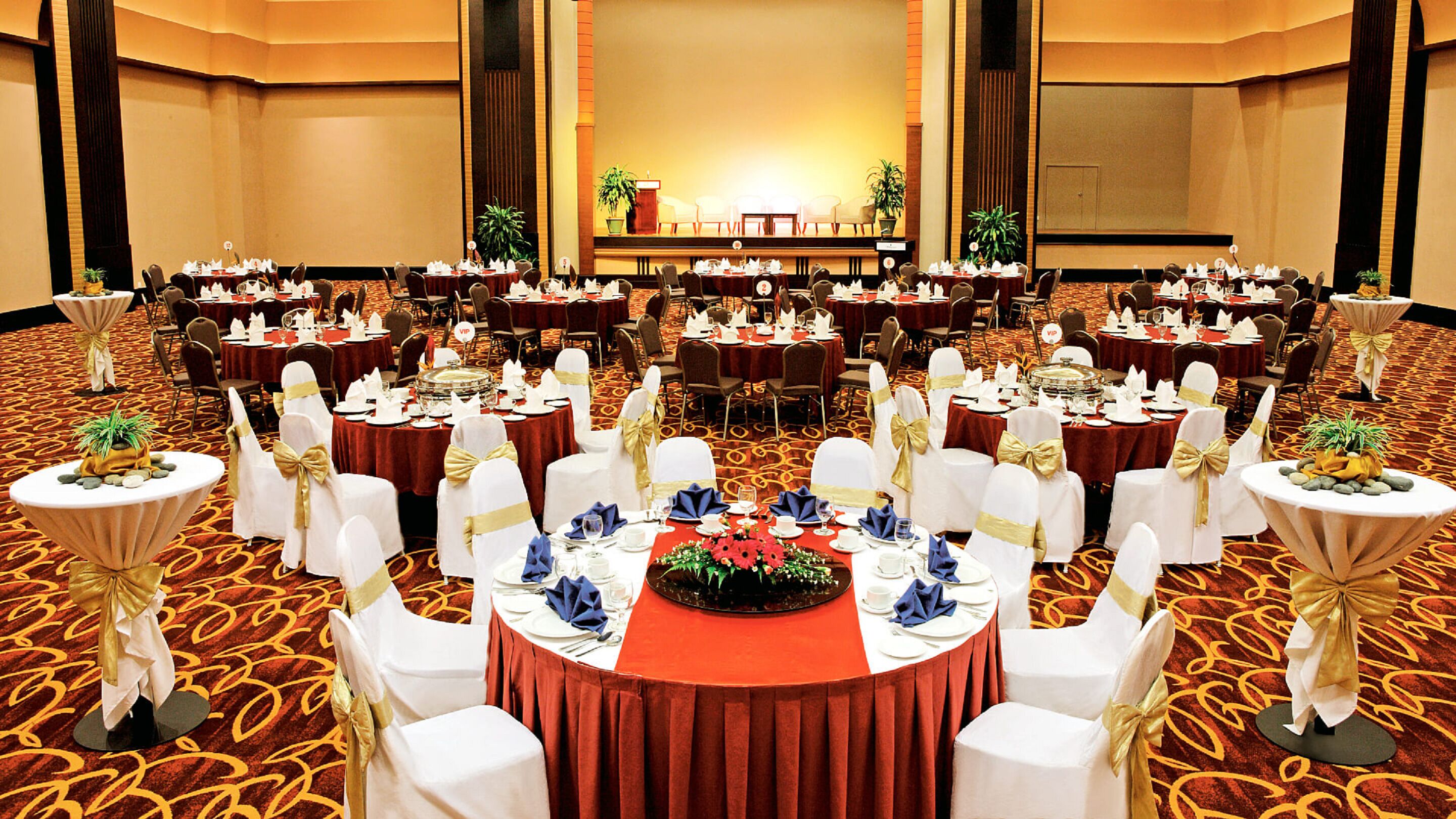 A banquet hall with round tables, white chairs, and red tablecloths.