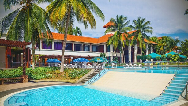 Un hotel con piscina, palmeras y un edificio de techo rojo.