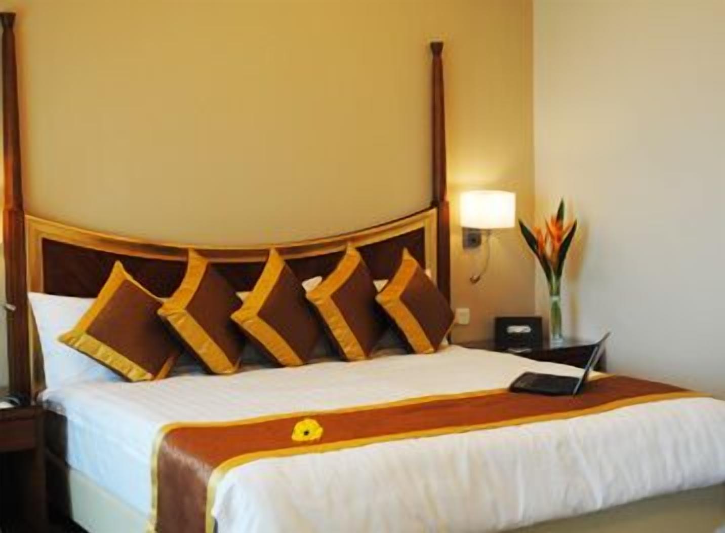 A hotel room with a bed, a nightstand, a lamp, and a vase with flowers.