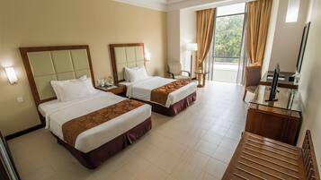 A hotel room with two beds, a desk, a chair, a TV, and a window with curtains.
