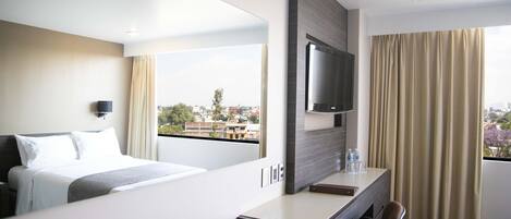 A hotel room with a bed, a desk, a chair, a TV, and a window with curtains.