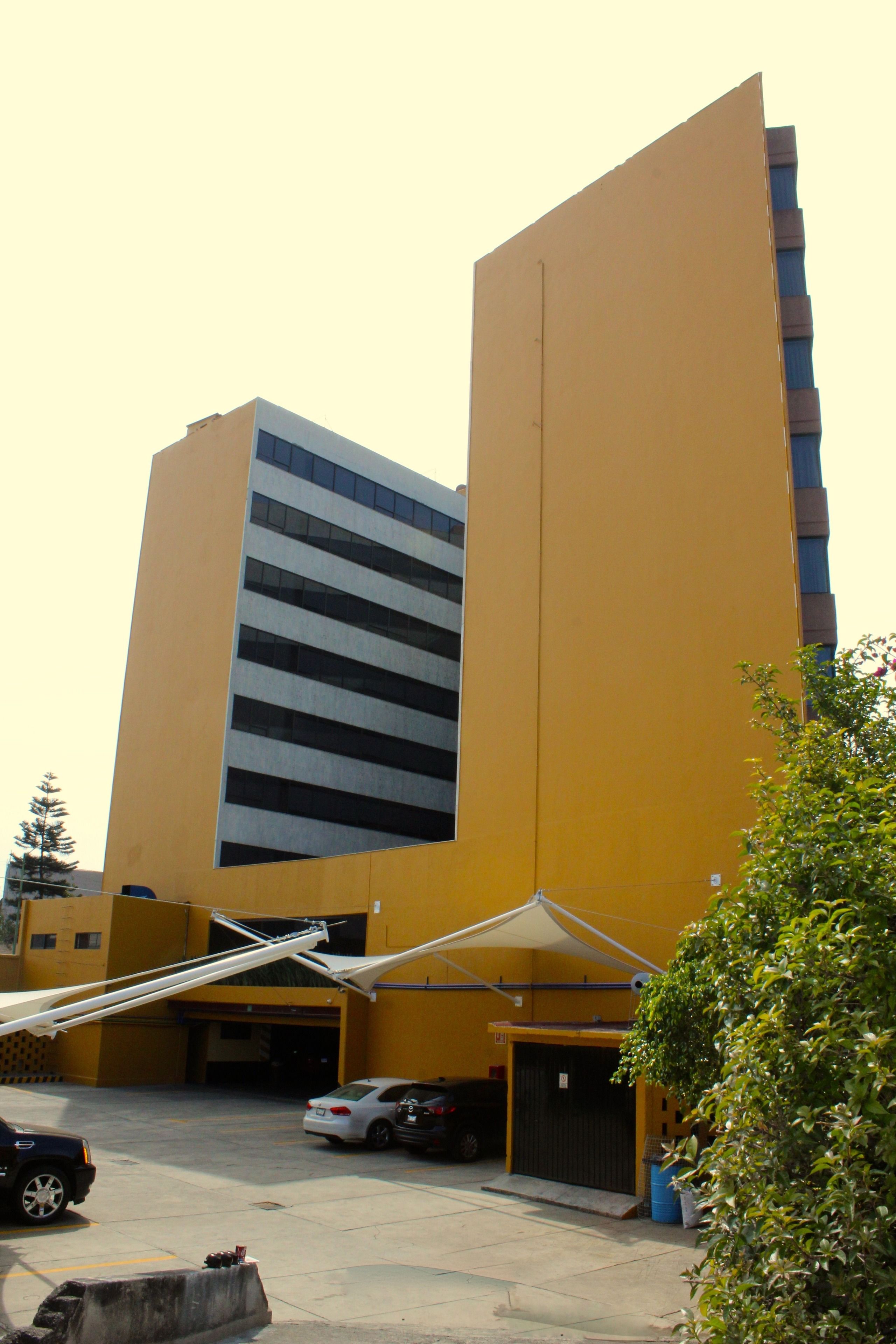 A yellow building with a modern design, featuring a parking area with several cars and a covered entrance.