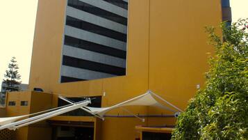 A yellow building with a modern design, featuring a parking area with several cars and a covered entrance.