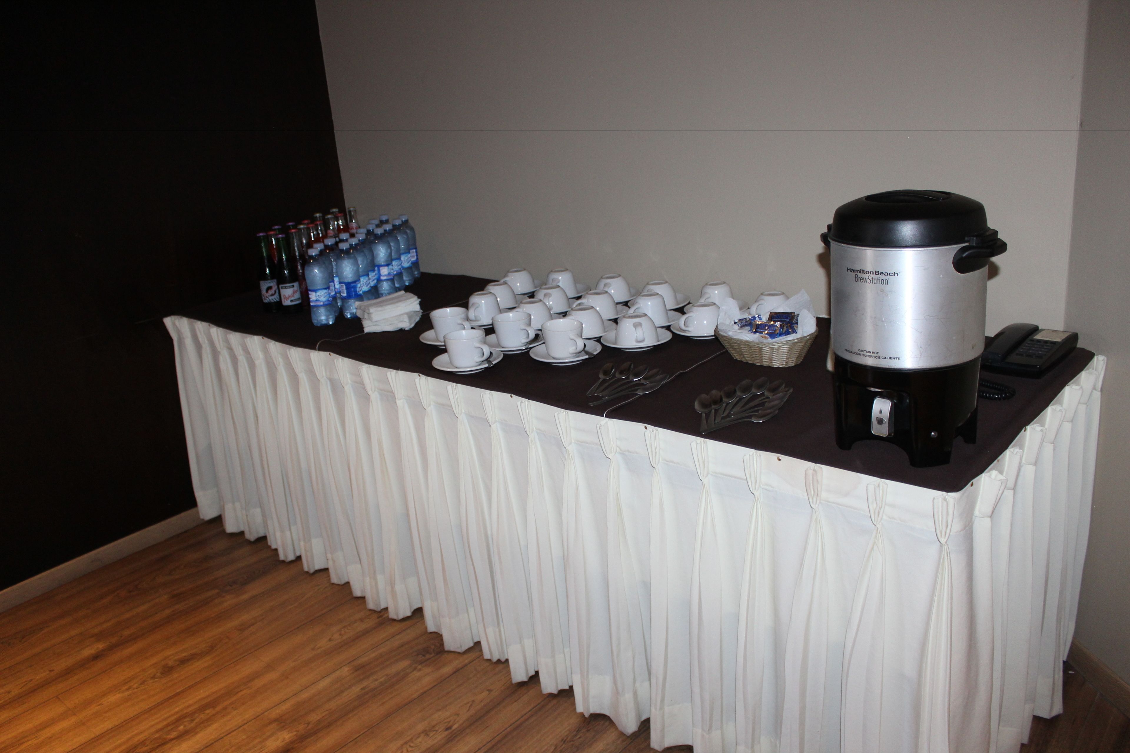 A buffet table with a coffee maker, water bottles, and disposable cups.