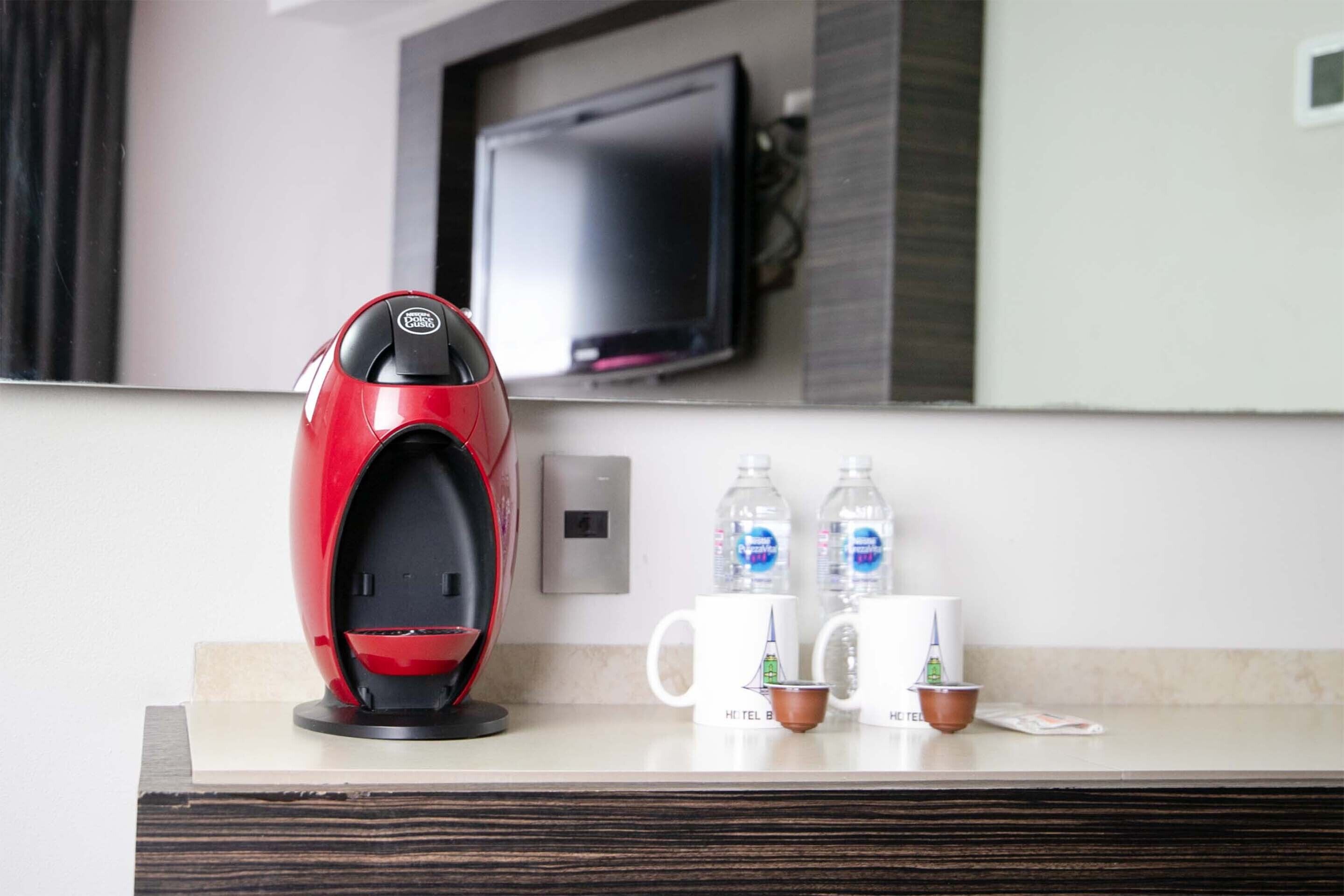 A modern hotel room with a coffee maker, two water bottles, and two mugs on the counter.