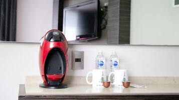 A modern hotel room with a coffee maker, two water bottles, and two mugs on the counter.