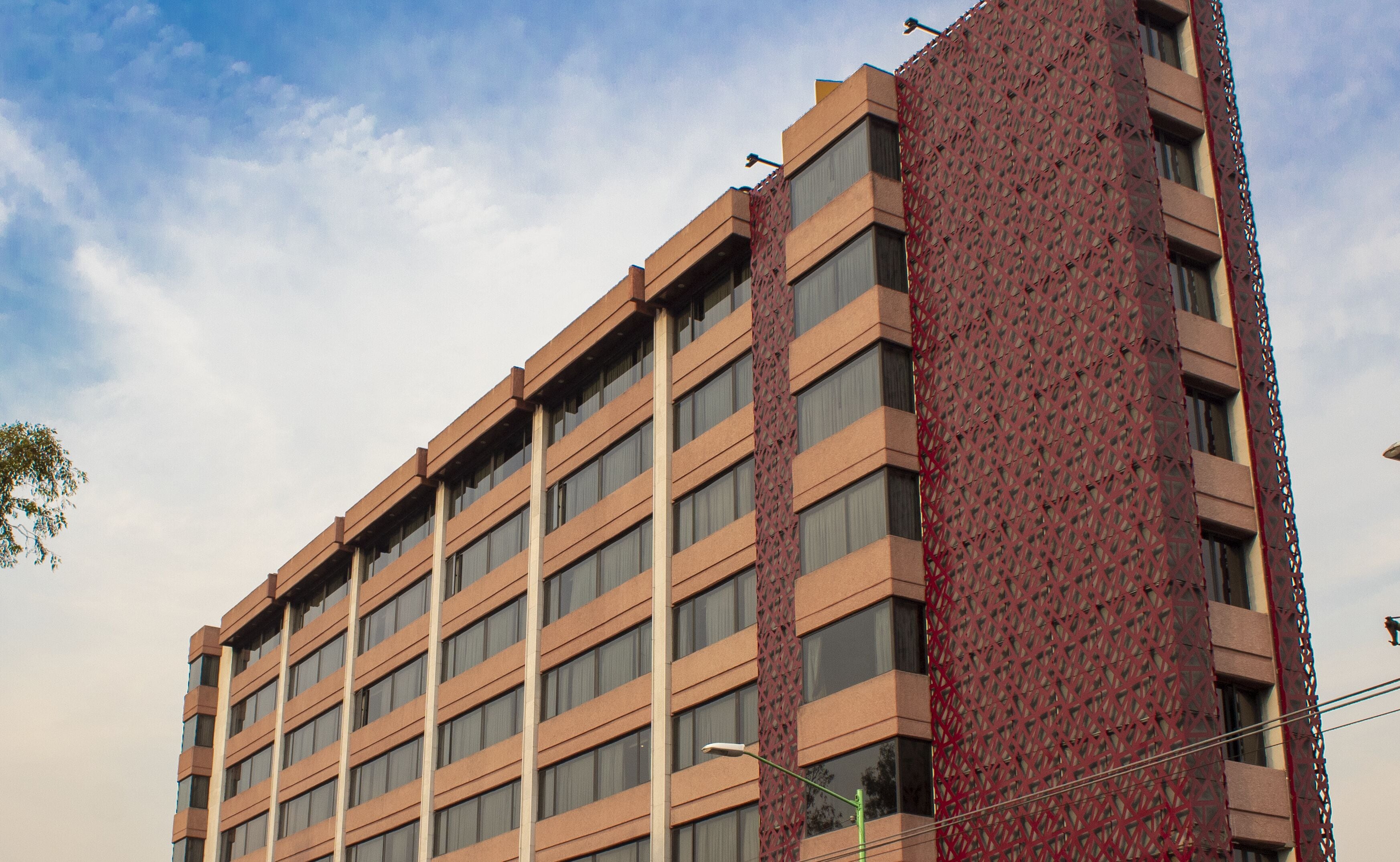 A multi-story building with a distinctive red lattice facade on one side, large windows, and a flat roof.