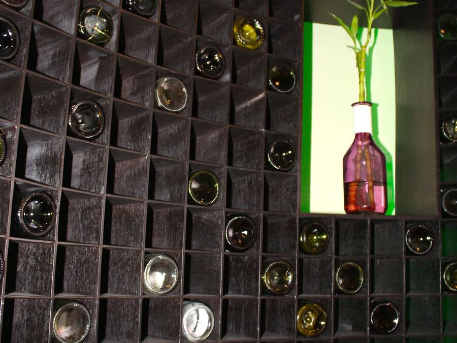 A wall with a grid of square panels, some containing clear glass bottles.