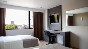 Habitación de hotel con dos camas, un escritorio con silla, televisión y un ventanal con cortinas.