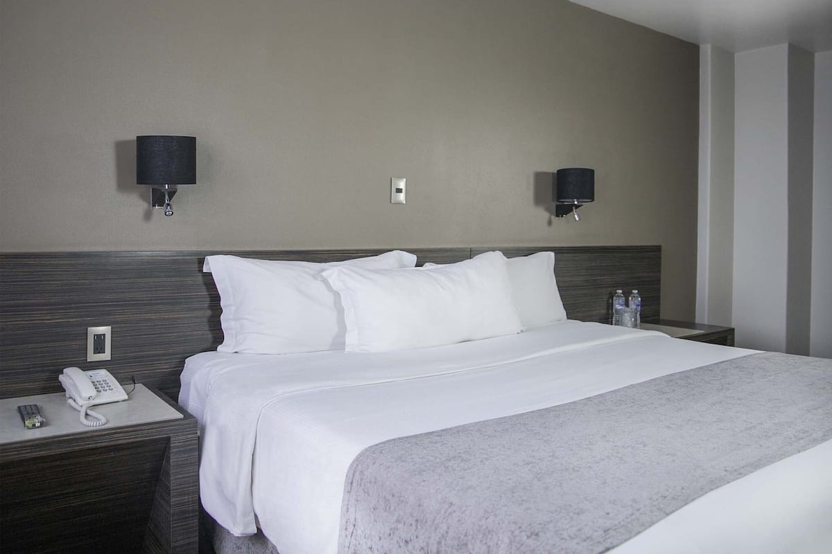 A hotel room with a large bed, two bedside tables, a phone, and two wall-mounted lamps.