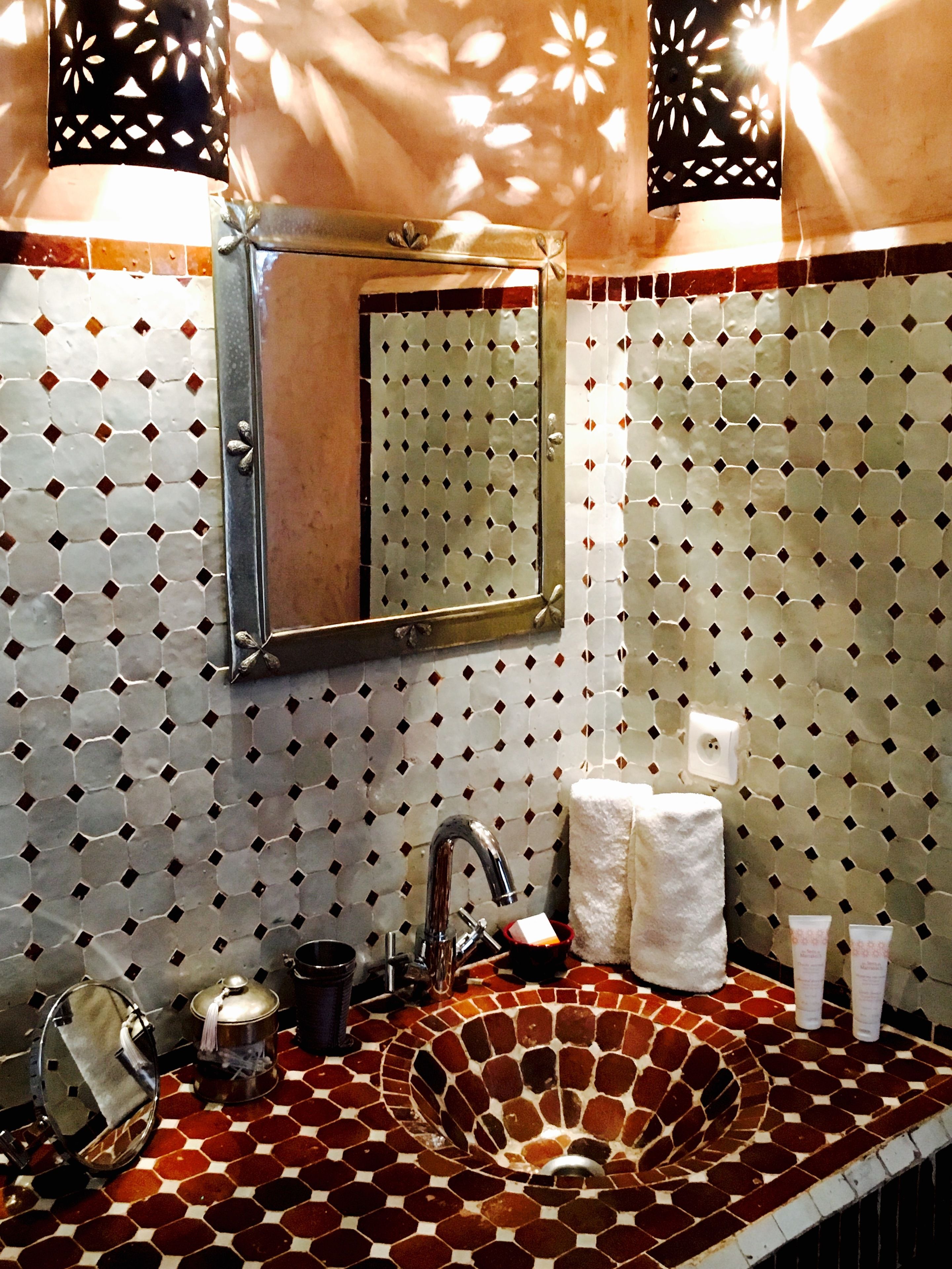 A bathroom with a hexagonal patterned tile backsplash, a round sink with a faucet, a mirror, and a towel rack.