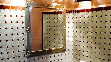 Un baño con salpicadero de azulejos de patrón hexagonal, un lavabo redondo con grifo, un espejo y un perchero.