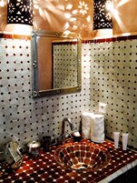 Un baño con salpicadero de azulejos de patrón hexagonal, un lavabo redondo con grifo, un espejo y un perchero.