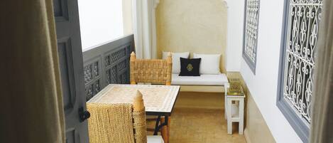 A room with a wooden table, two wicker chairs, a small white sofa, and a decorative wall panel.