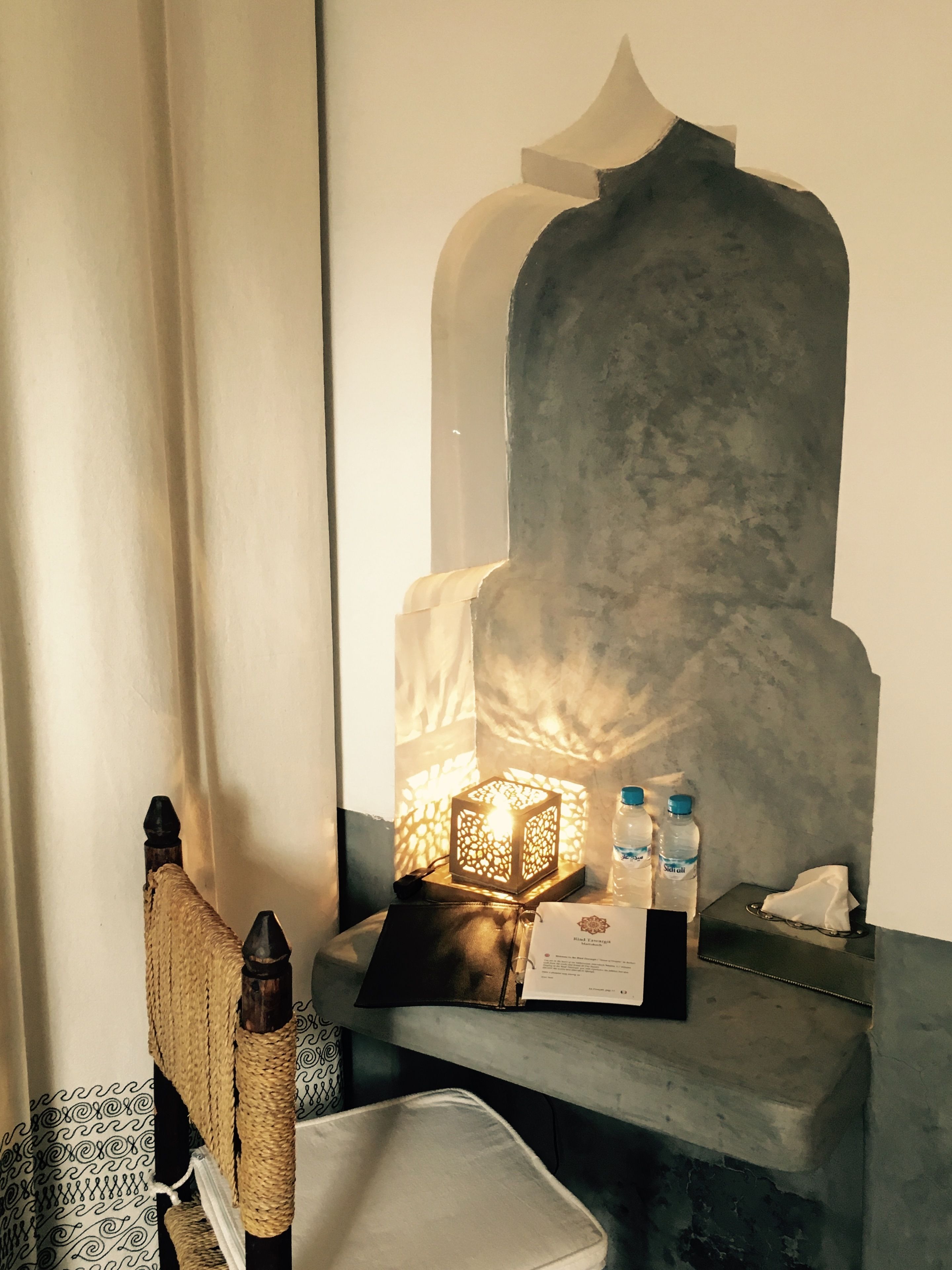 A bathroom with a mirror, a decorative lamp, a towel, a bottle of water, and a tissue.
