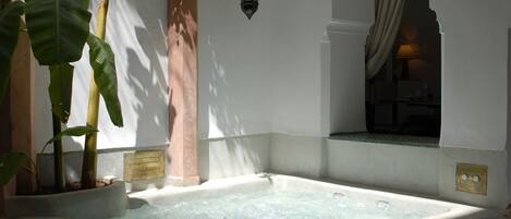 Un área de spa con un jacuzzi, plantas grandes en macetas y un farol de pared.