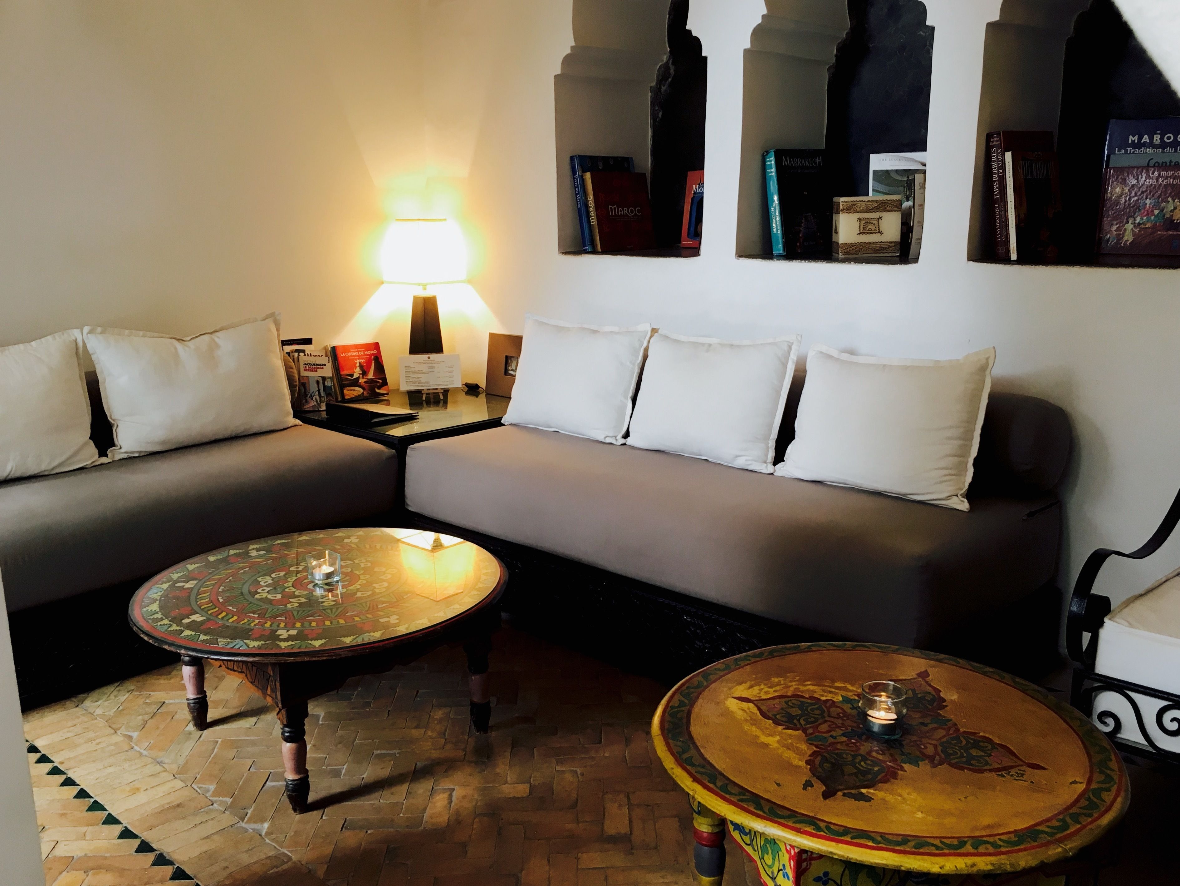 A modern living room with a sofa, two round tables, a lamp, and a bookshelf with books.