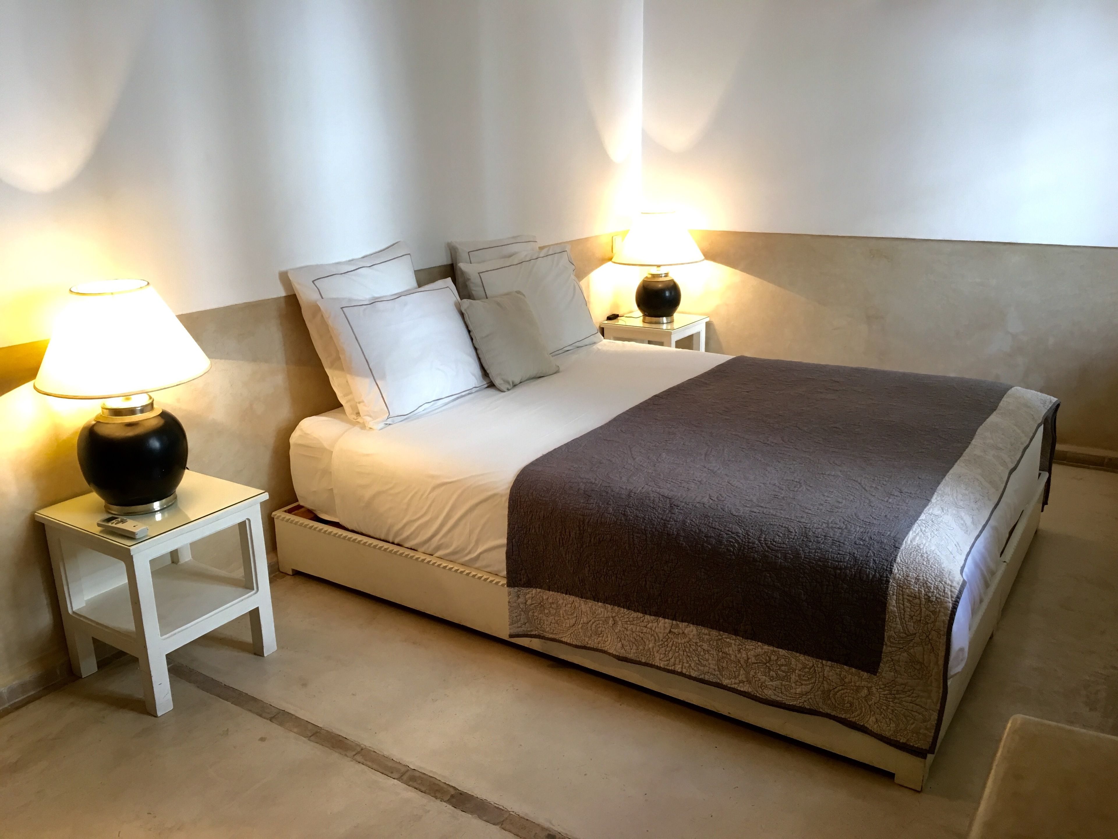 A neatly made bed with a white and brown bedspread, two bedside lamps, and a white nightstand.