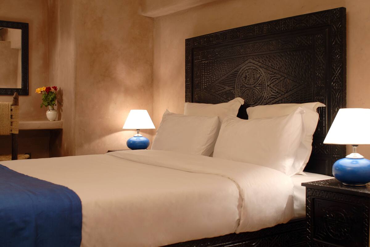 A neatly made bed with white linens and blue accents, a dark wooden headboard, and two bedside lamps with blue bases.