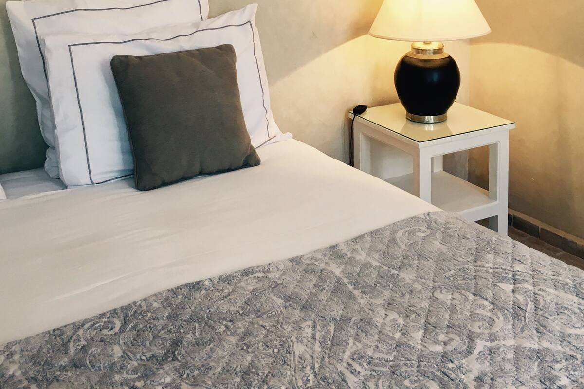 A neatly made bed with pillows, a bedside lamp, and a patterned rug.