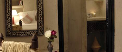 A room with a woven chair, a mirror with a decorative frame, and a vase with flowers.
