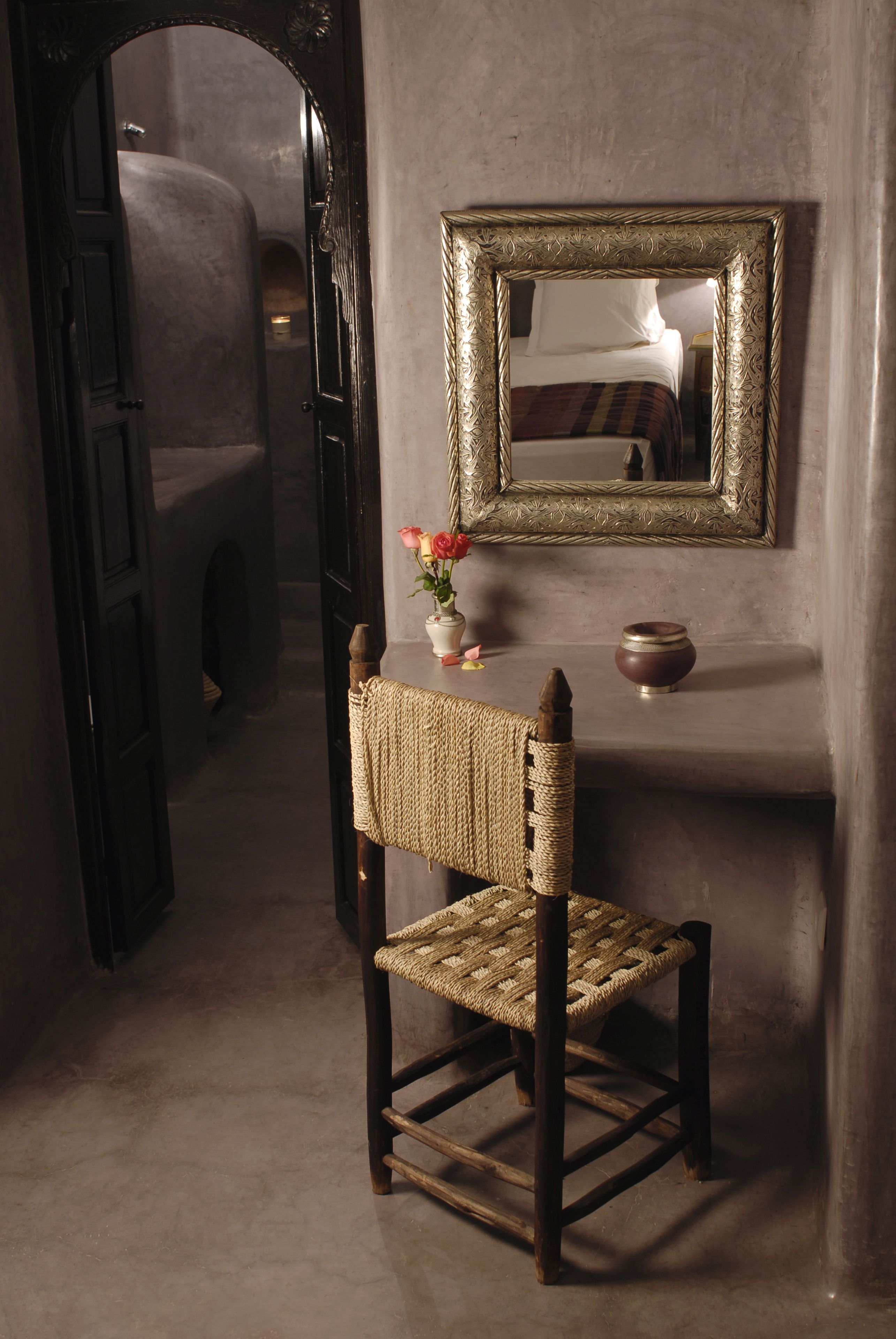 A rustic room with a woven chair, a mirror, and a vase with flowers.