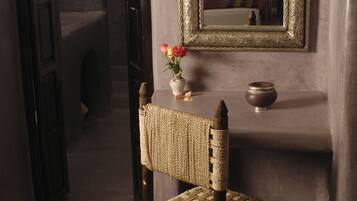 A rustic room with a woven chair, a mirror, and a vase with flowers.
