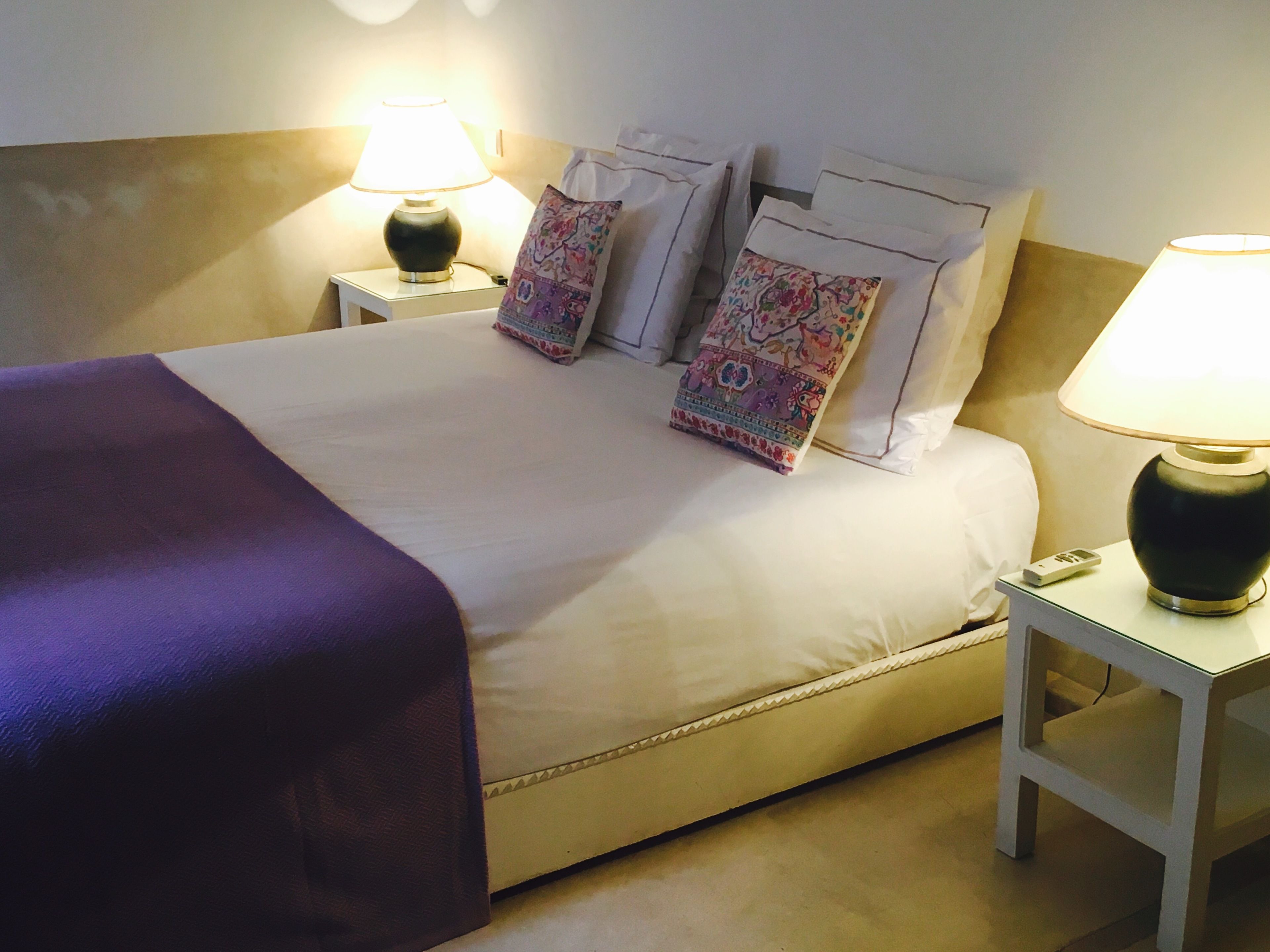A neatly made bed with a purple throw blanket, two bedside lamps, and decorative pillows.