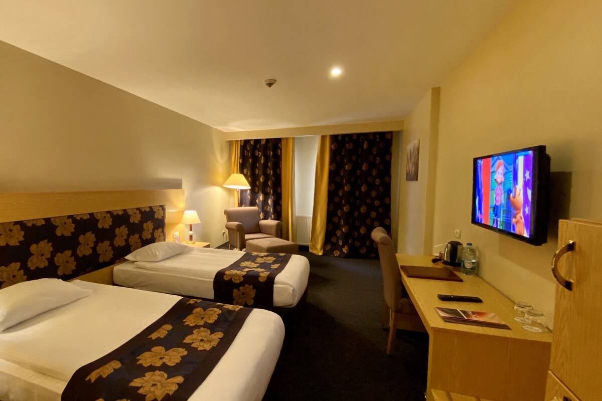 A hotel room with two beds, a desk, a television, and a chair.