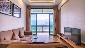 Een moderne woonkamer met een bank, salontafel en televisie. Grote ramen bieden uitzicht op het omliggende landschap.