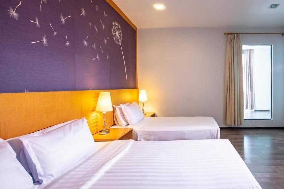 Quarto de hotel com duas camas, uma janela grande e uma parede com padrão de dentes-de-leão.