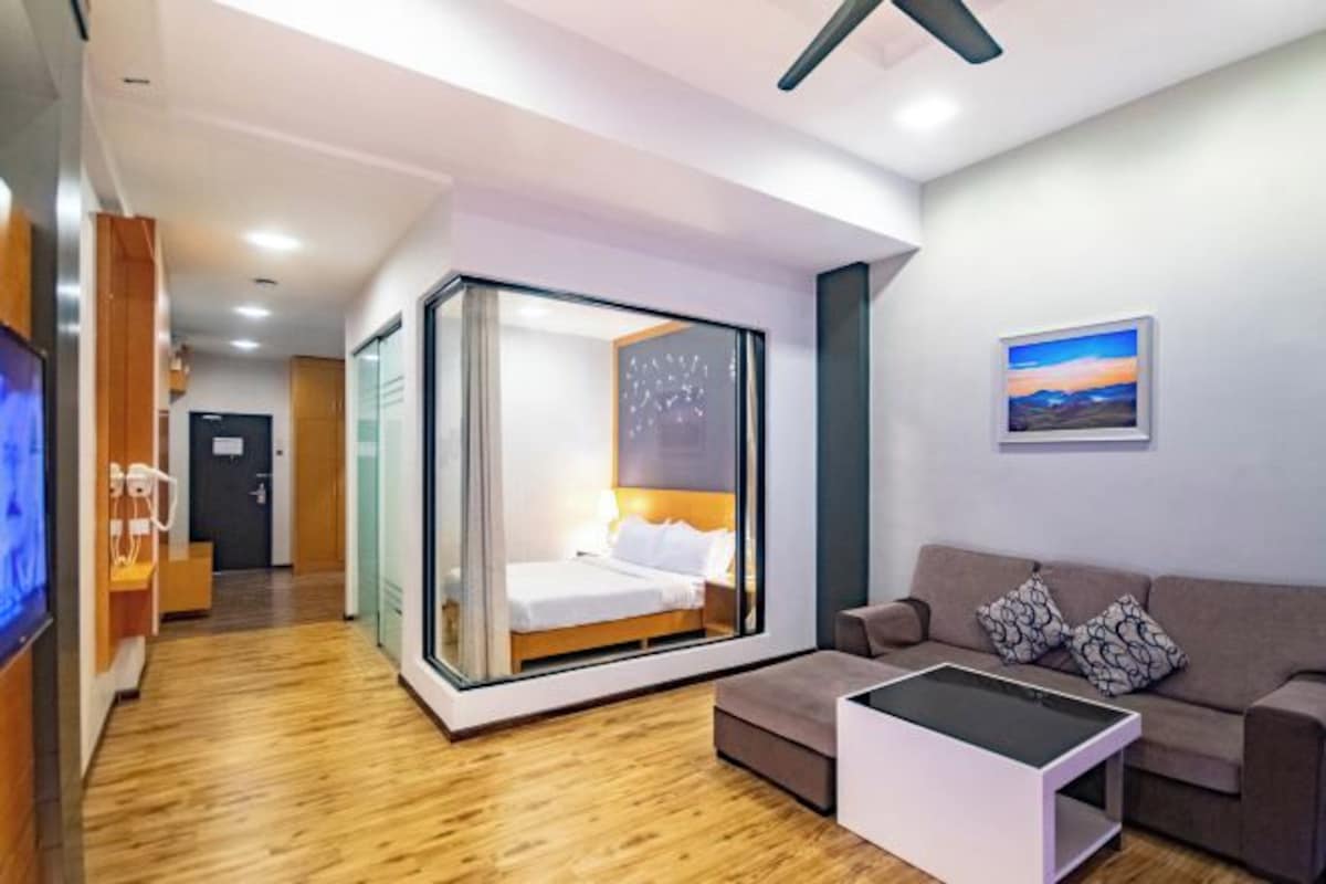 A modern hotel room with a glass-enclosed bed, a sofa, and a flat-screen TV.