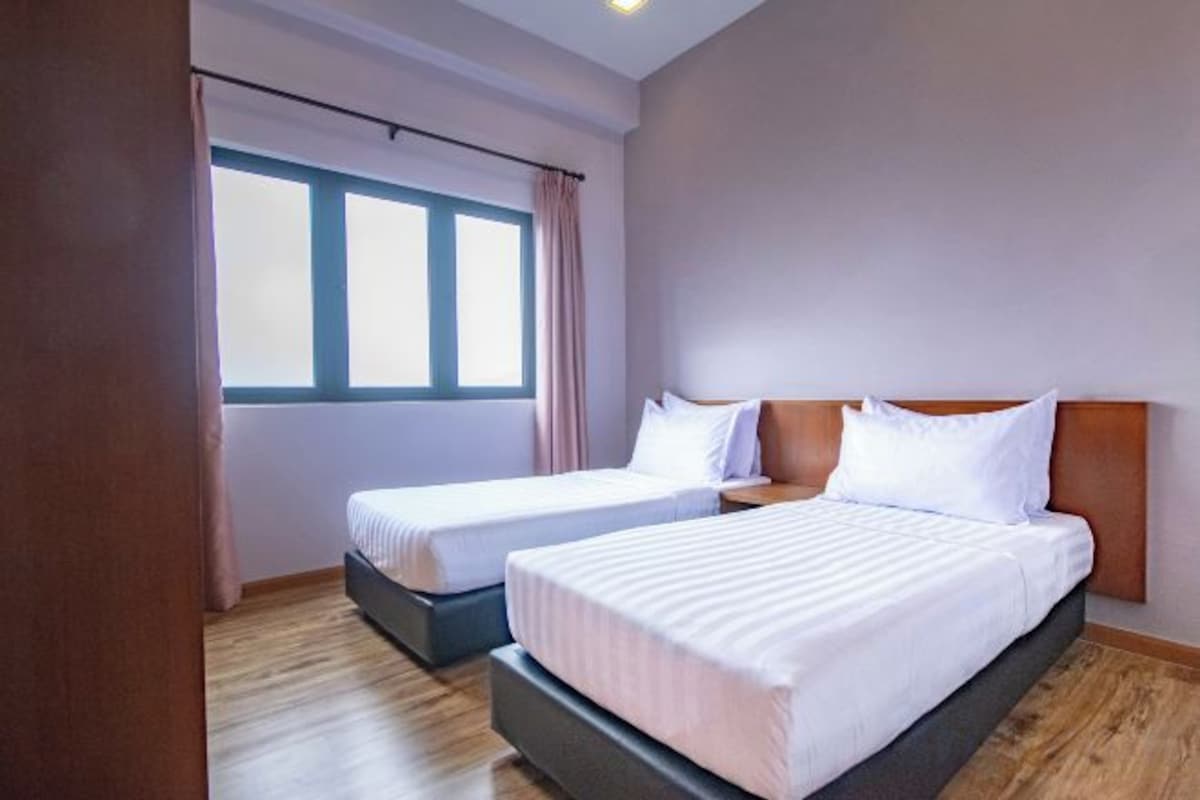 Una habitación de hotel con dos camas, un ventanal con cortinas y suelo de madera.