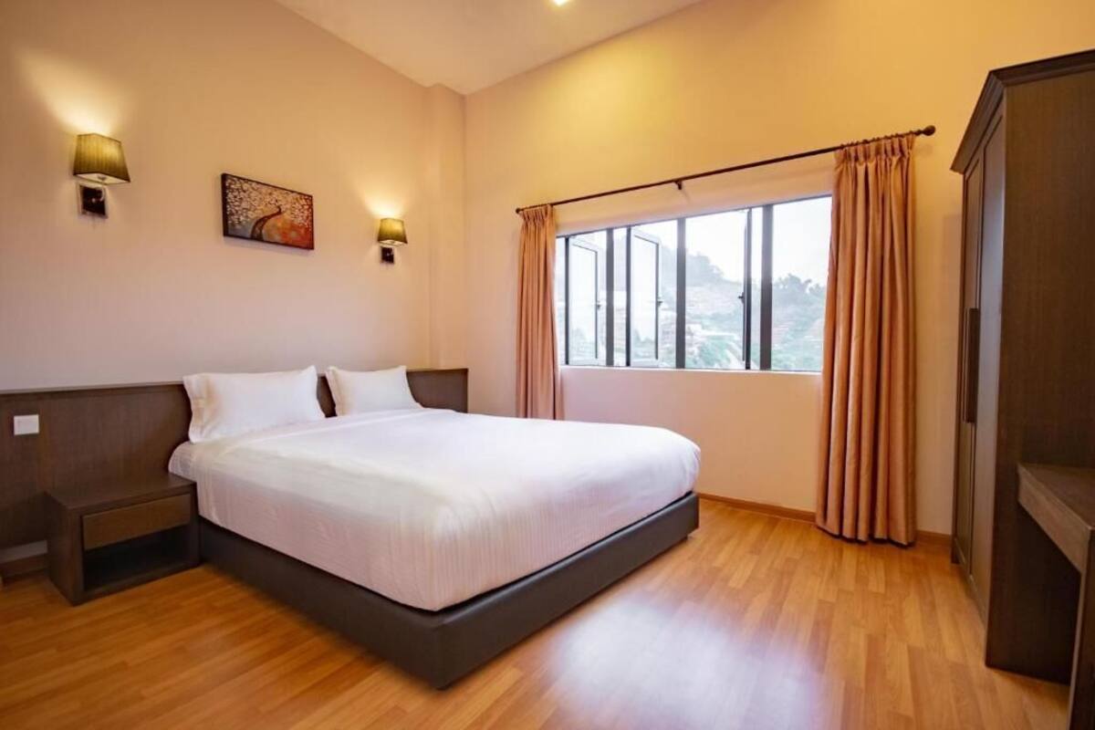 Quarto de hotel com uma cama grande, uma mesa de cabeceira, uma janela com cortinas e luminárias fixadas na parede.