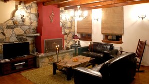 Ein gemütliches Wohnzimmer mit Kamin aus Stein, Ledersofa und Holzbalken an der Decke.