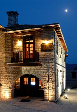 Un edificio de piedra con un balcón, una entrada iluminada y un letrero sobre la puerta.