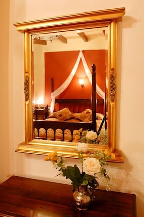 A bedroom with a four-poster bed, a mirror with a gold frame, and a vase with flowers on a wooden dresser.