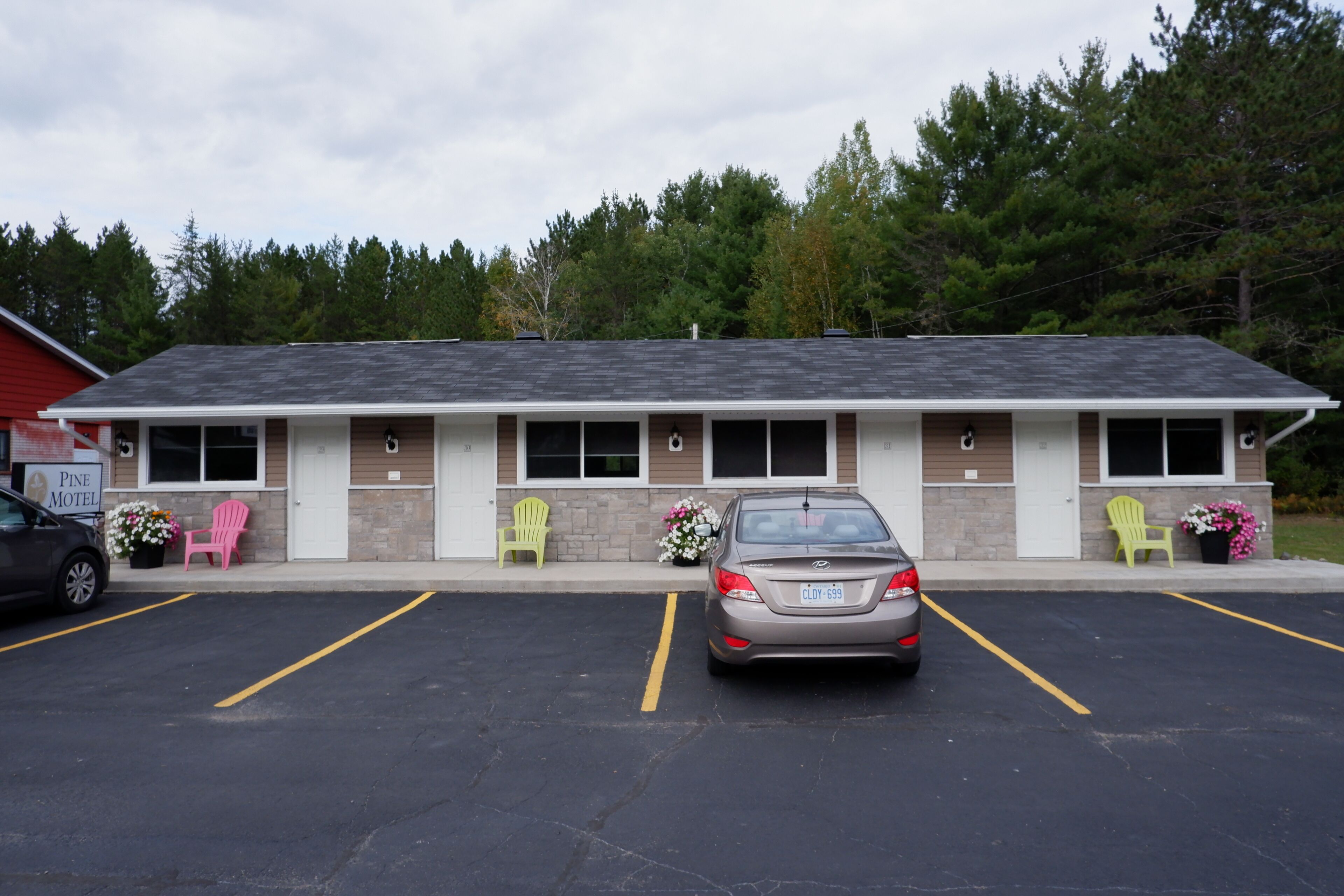 Un motel avec un parking, deux chaises vertes et une voiture garée devant.