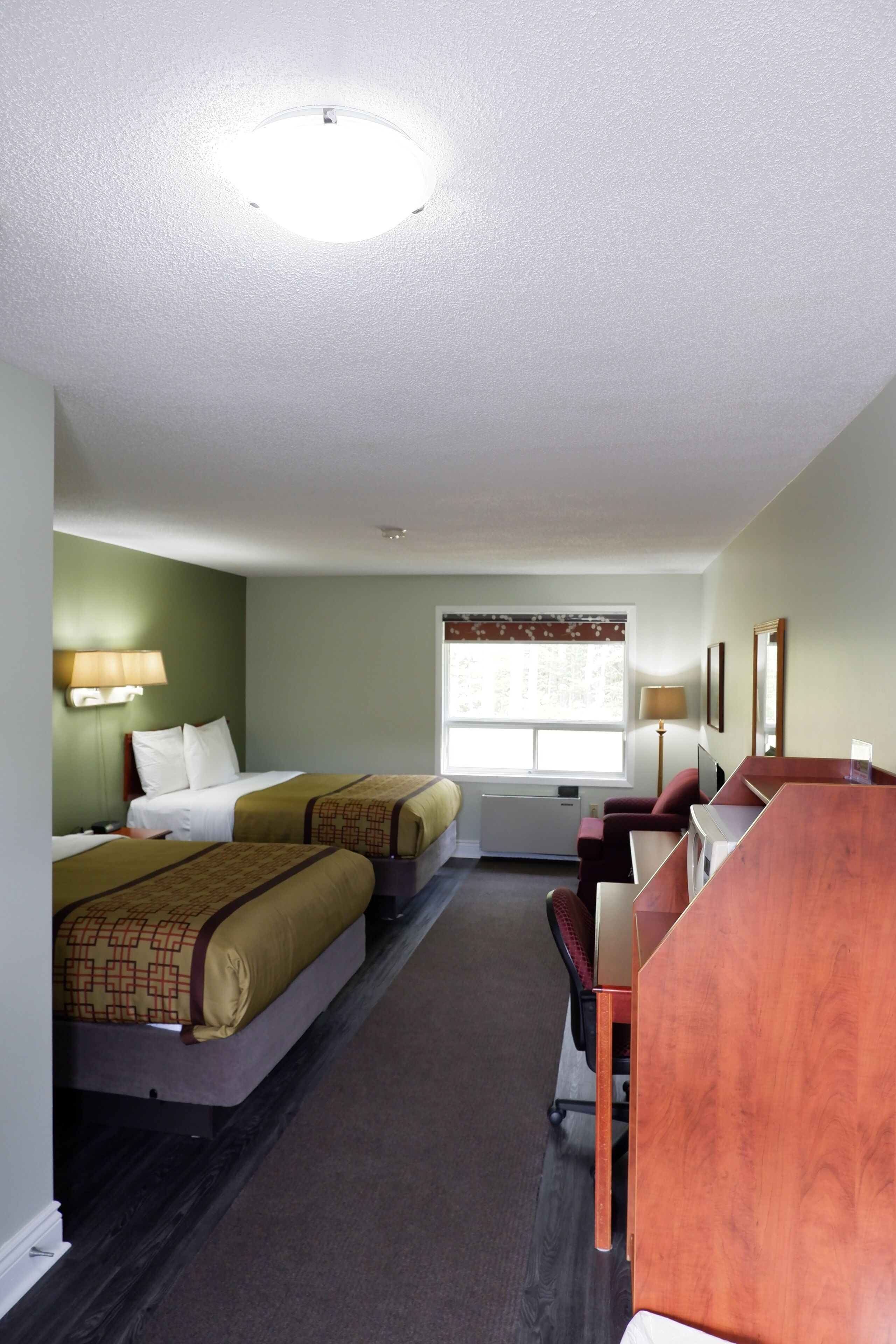 A hotel room with two beds, a desk, a chair, a window with a view, and a ceiling light.