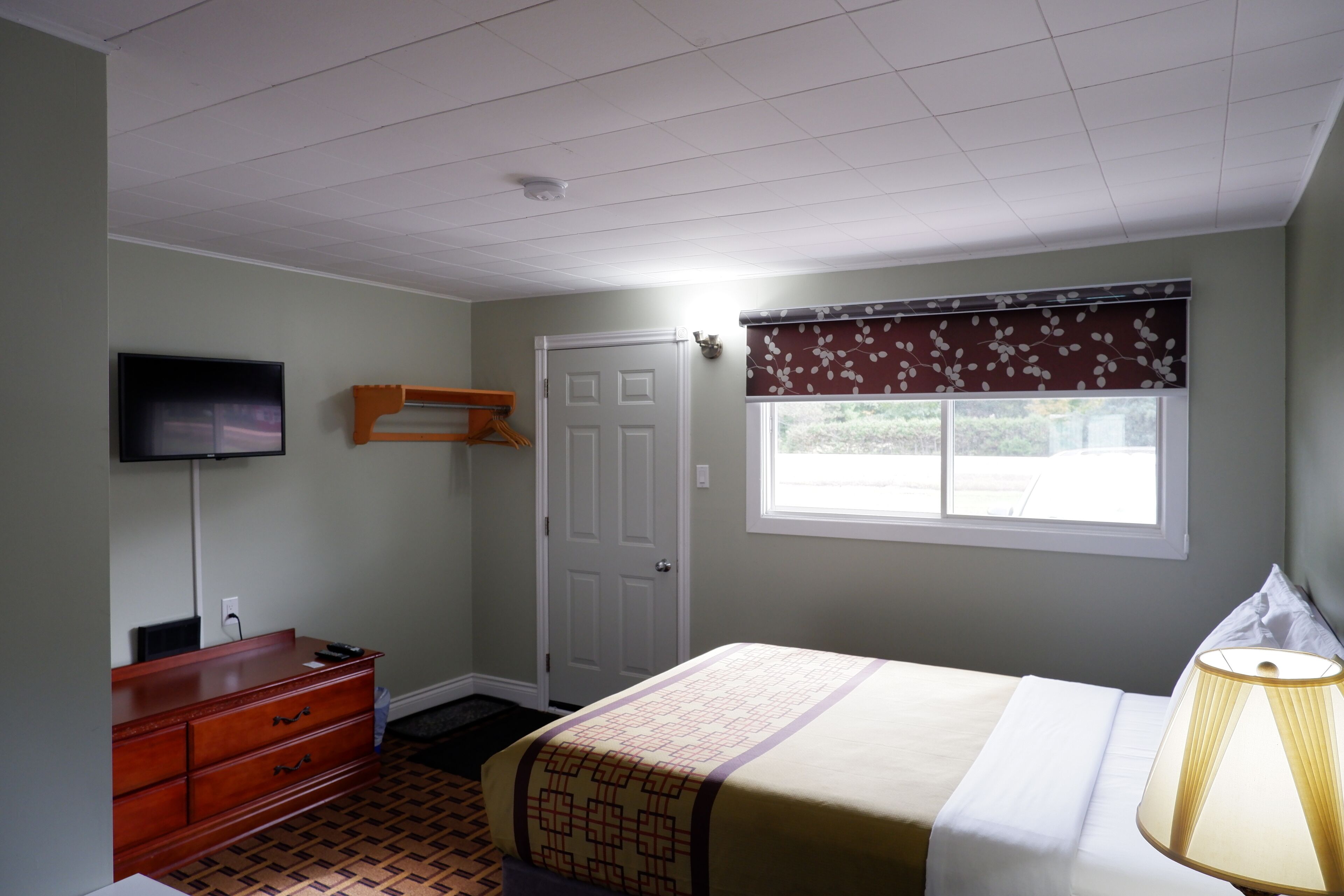 Un dormitorio con cama, cómoda, televisor, puerta y ventana con vistas.