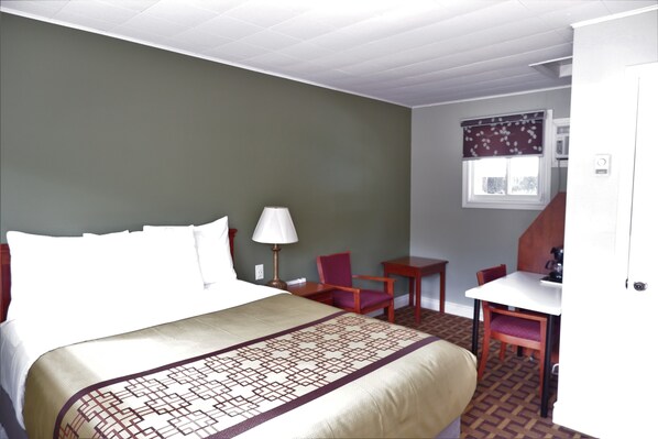 Habitación de hotel con cama, escritorio, silla y ventana con cortina.