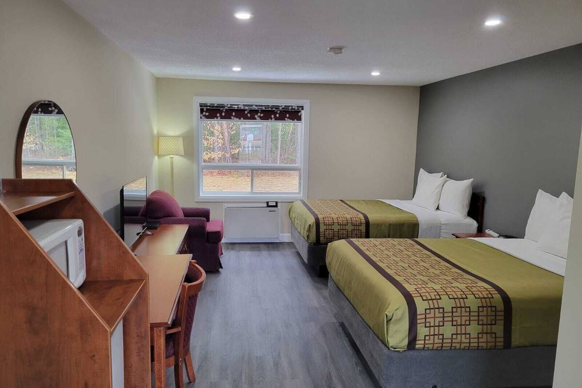 Habitación de hotel con dos camas, un escritorio, una silla, un espejo y una ventana con vistas a árboles.