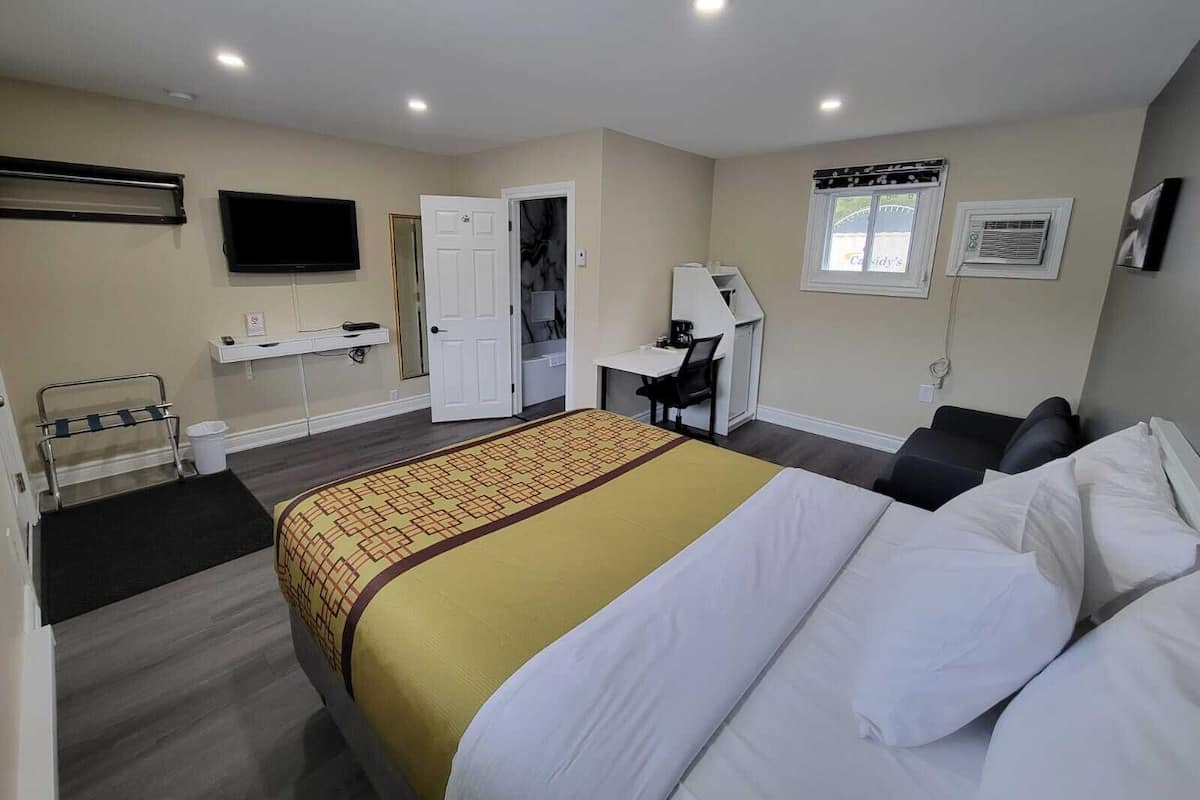 Una habitación de hotel con cama, escritorio, silla, televisor y ventana.