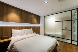 A modern bedroom with a wooden headboard, a large bed, a nightstand, and a glass partition wall.