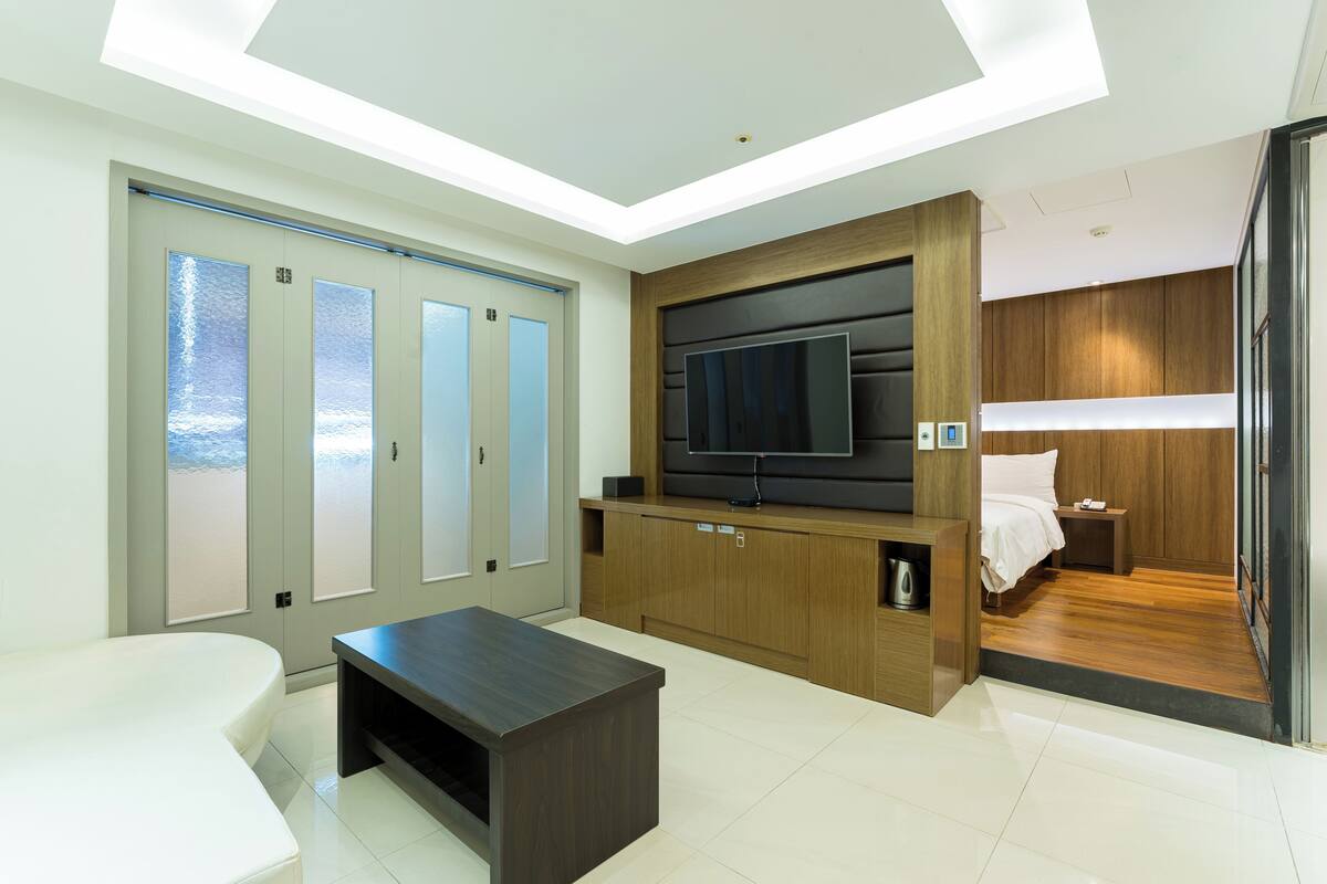 A modern hotel room with a large flat-screen TV, a sofa, a coffee table, and a bed.