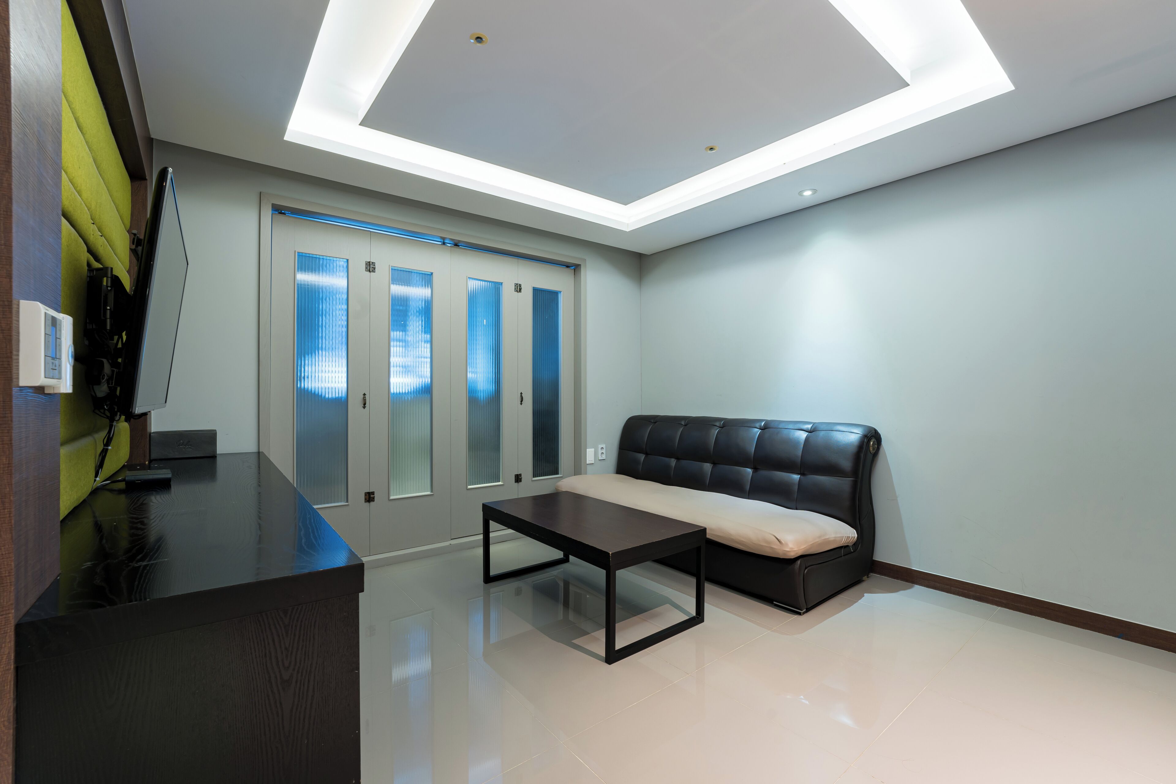 A modern lobby with a reception desk, a black leather sofa, and a glass elevator.