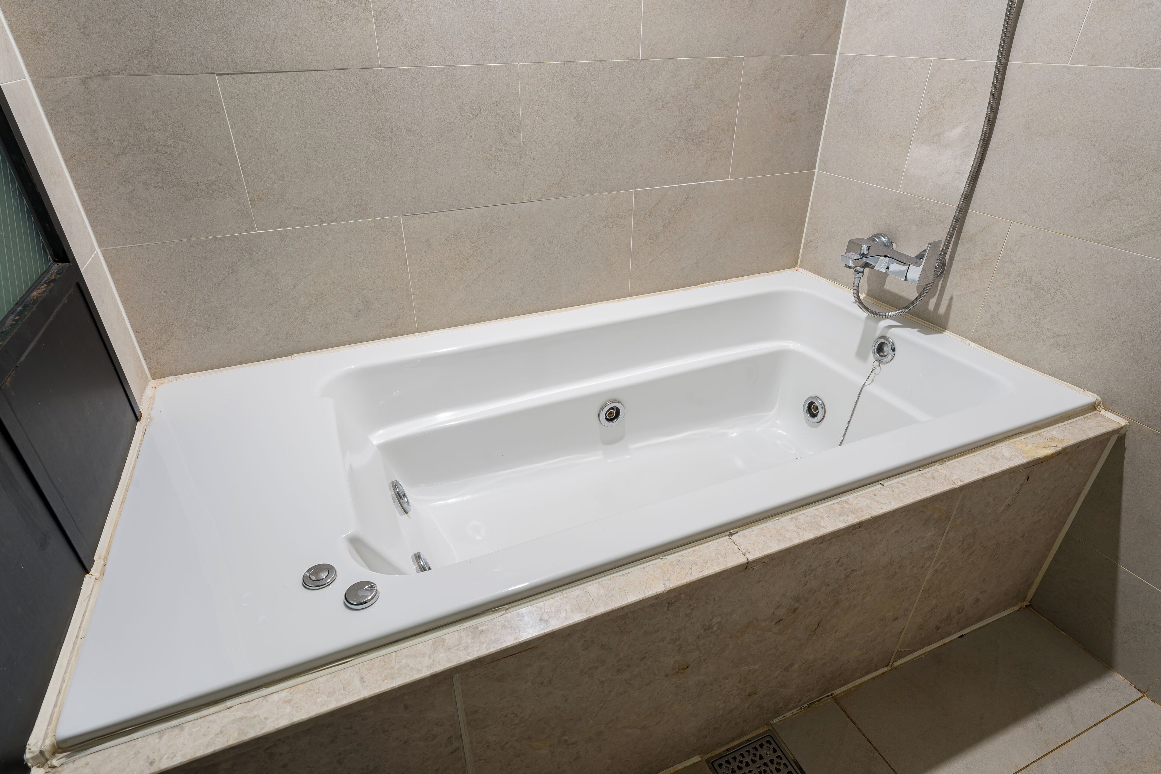 A modern bathroom with a white bathtub, a showerhead, and a tiled wall.