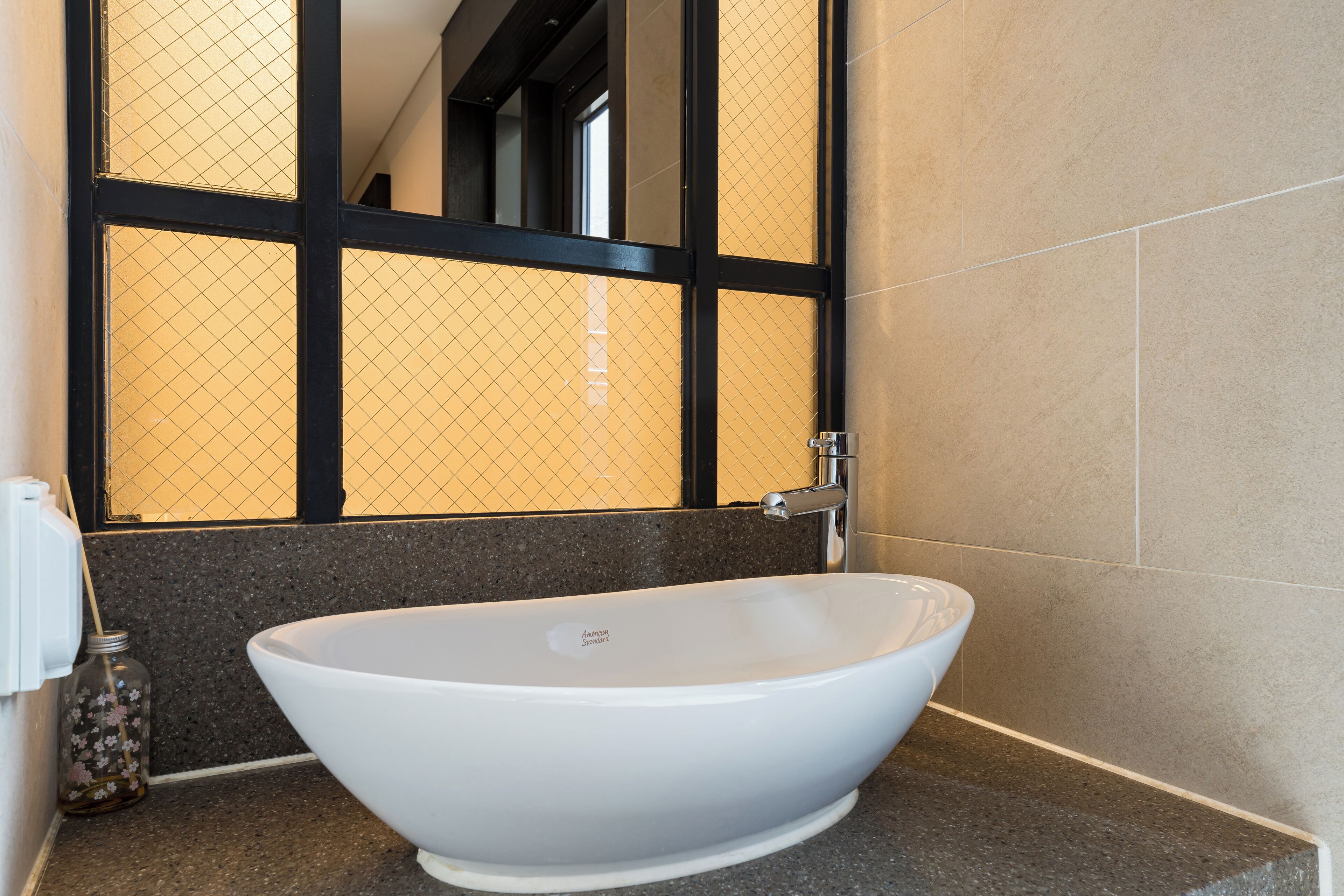 A modern bathroom with a freestanding white bathtub, a dark tiled wall, and a window with a black frame.