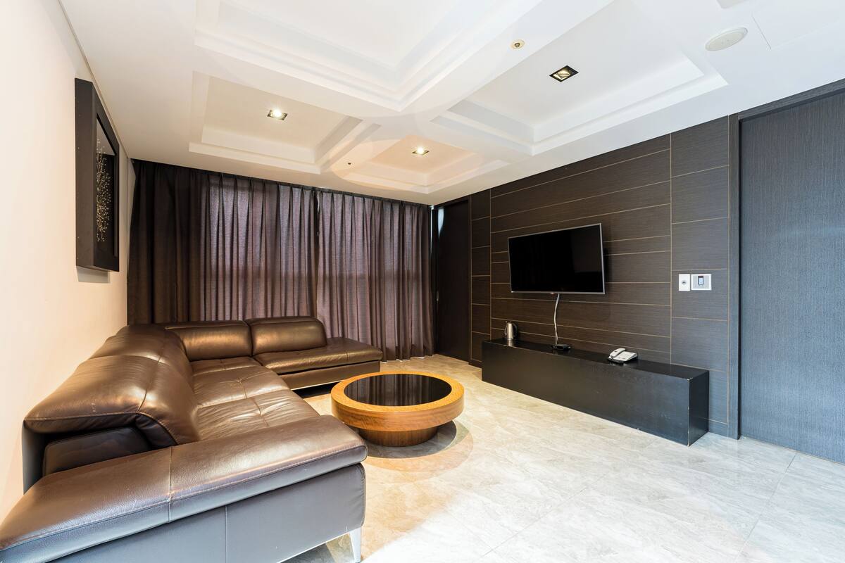 A modern living room with a sectional sofa, a round coffee table, a flat-screen TV mounted on the wall, and a dark accent wall.