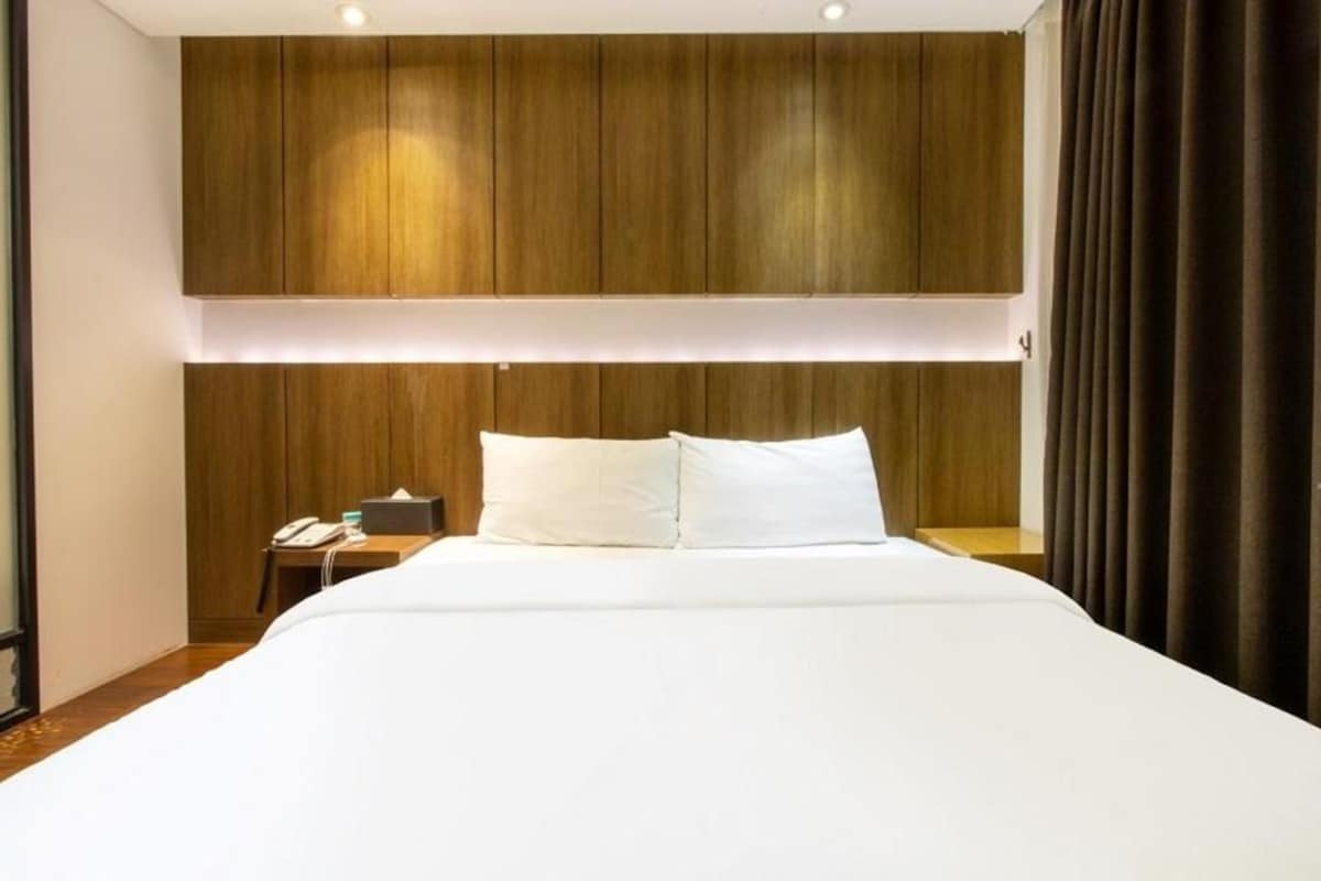 A hotel room with a large bed, wooden headboard, bedside table with a phone, and a curtain on the right.